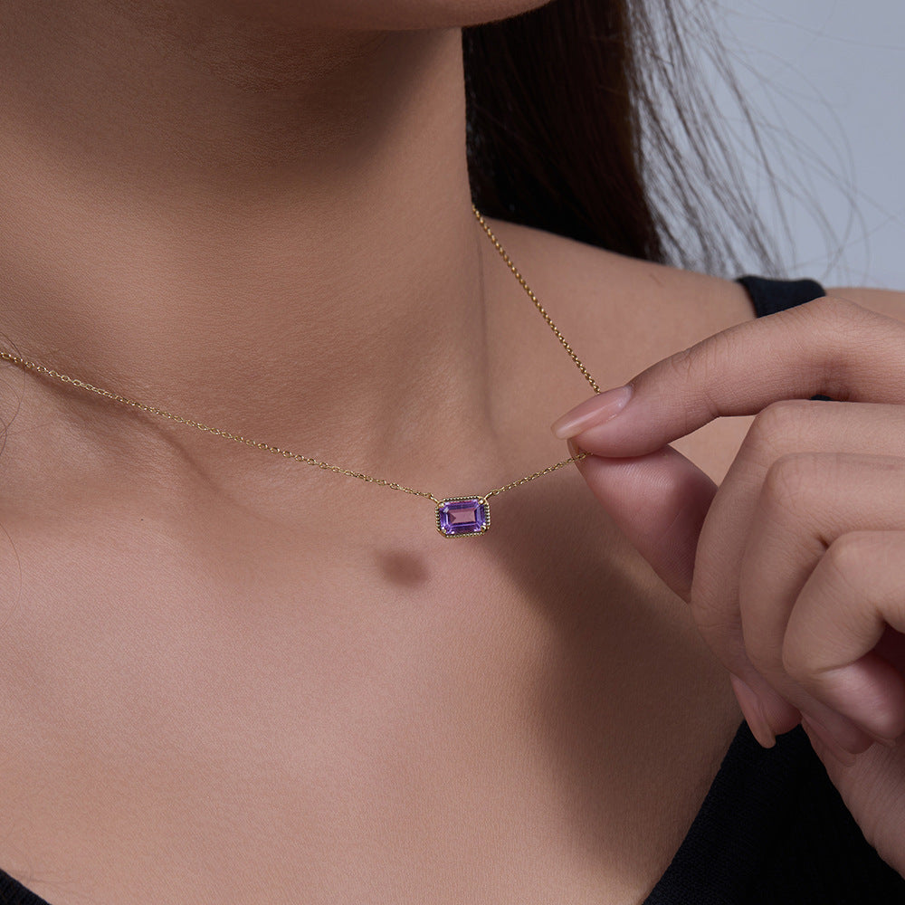 Close-up of woman holding gold colored S925 amethyst pendant necklace against skin.