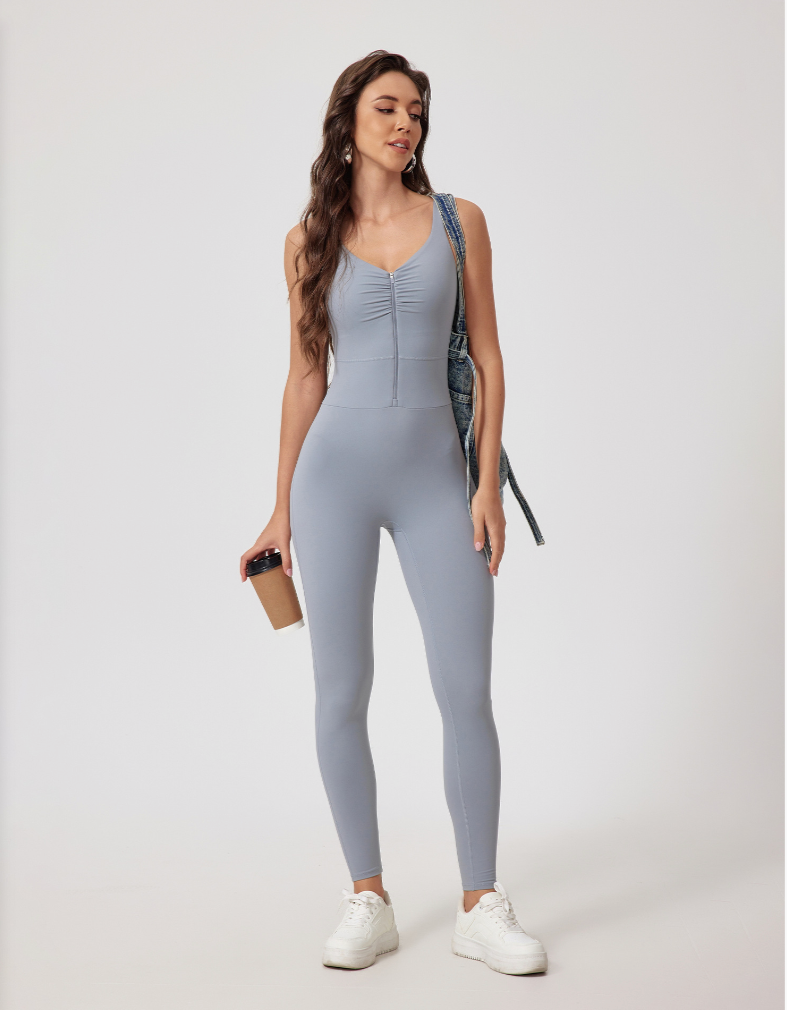 A woman wearing a light gray fitted jumpsuit with front zip detail, posing with coffee cup against white background
