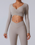A model wearing a light taupe wrap-style crop top with long sleeves and matching leggings, featuring a V-shaped waistband detail against gray backdrop