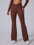 Chocolate brown flared yoga pants with V-shaped waistband and long sleeves, styled with white sneakers against gray backdrop