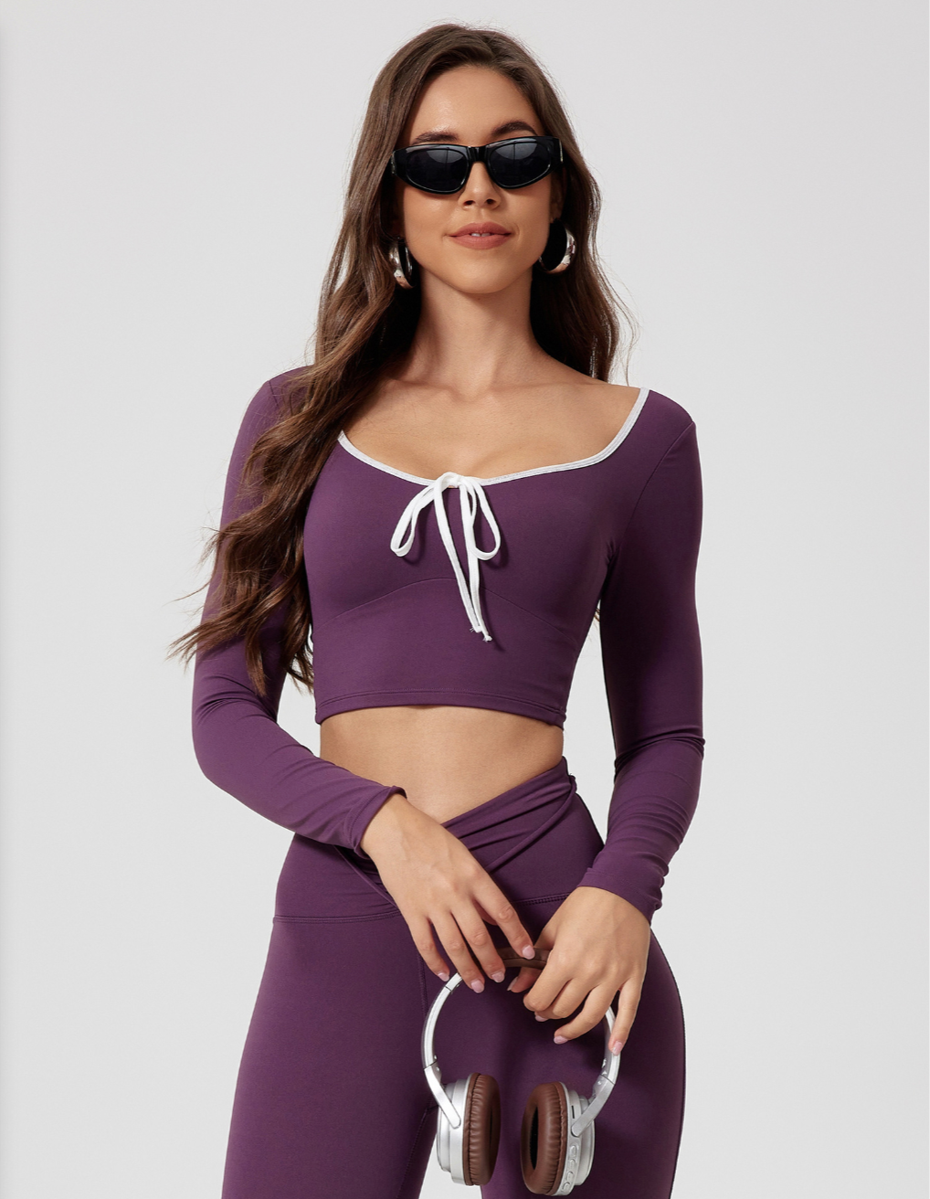 Purple workout set with long sleeve crop top and leggings, featuring white trim and front tie detail, styled with headphones and sunglasses, style CX2942