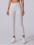 A model is standing wearing white high-waisted leggings with V-shaped waistband paired with white platform sneakers against neutral gray background