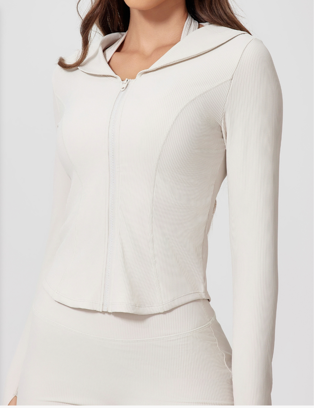 Close-up of woman wearing a cream ribbed zip-up jacket with hooded collar and fitted silhouette