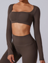 Model wearing dark brown ruched crop top with long sleeves and square neckline, paired with matching leggings against white backdrop