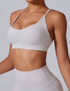 A woman wearing a white strappy sports bra with ruched center detail and matching high-waist leggings against neutral backdrop