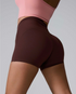High-waisted brown athletic shorts shown from side angle, paired with pink sports bra, against light gray background
