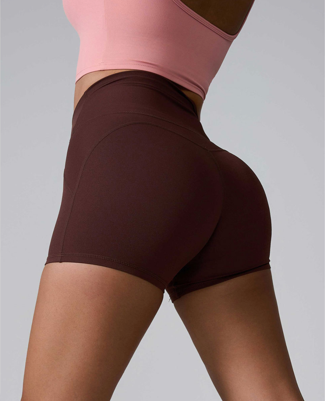 High-waisted brown athletic shorts shown from side angle, paired with pink sports bra, against light gray background