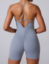 Back view of model showing powder blue bodysuit with T-strap back design and ruched detail against neutral background