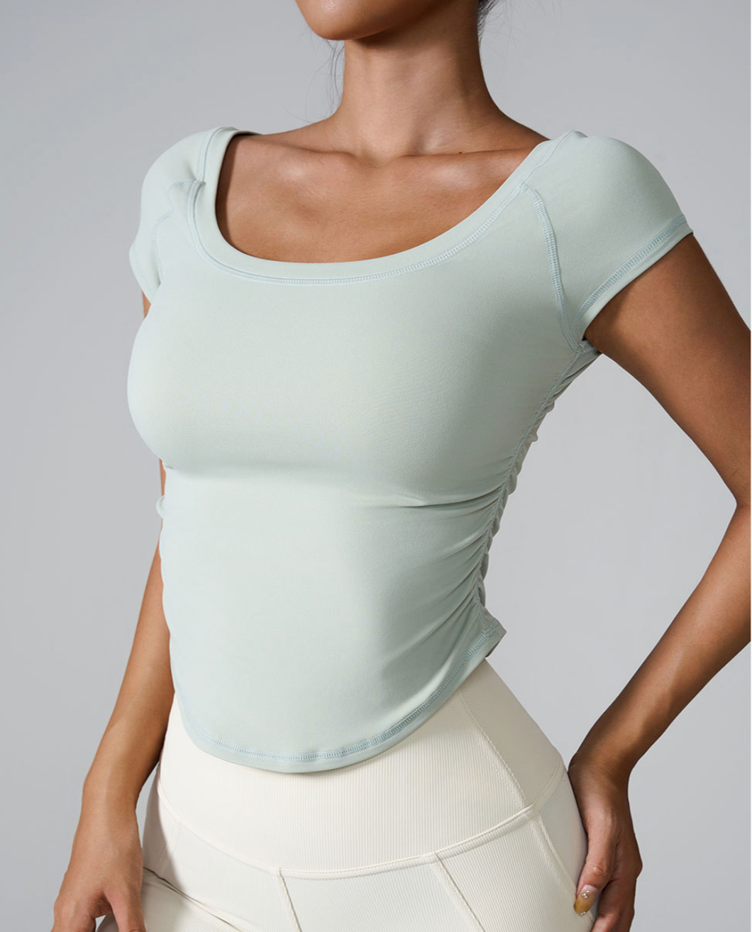 Model wearing mint green square-neck crop top with side ruching, paired with cream ribbed leggings against gray background