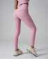 A model wearing pink high-waisted workout leggings with matching crop top, showing side profile against gray backdrop