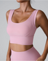 A woman wearing a light pink ribbed scoop neck sports bra with wide straps and supportive underbust band paired with matching bottoms against a gray background