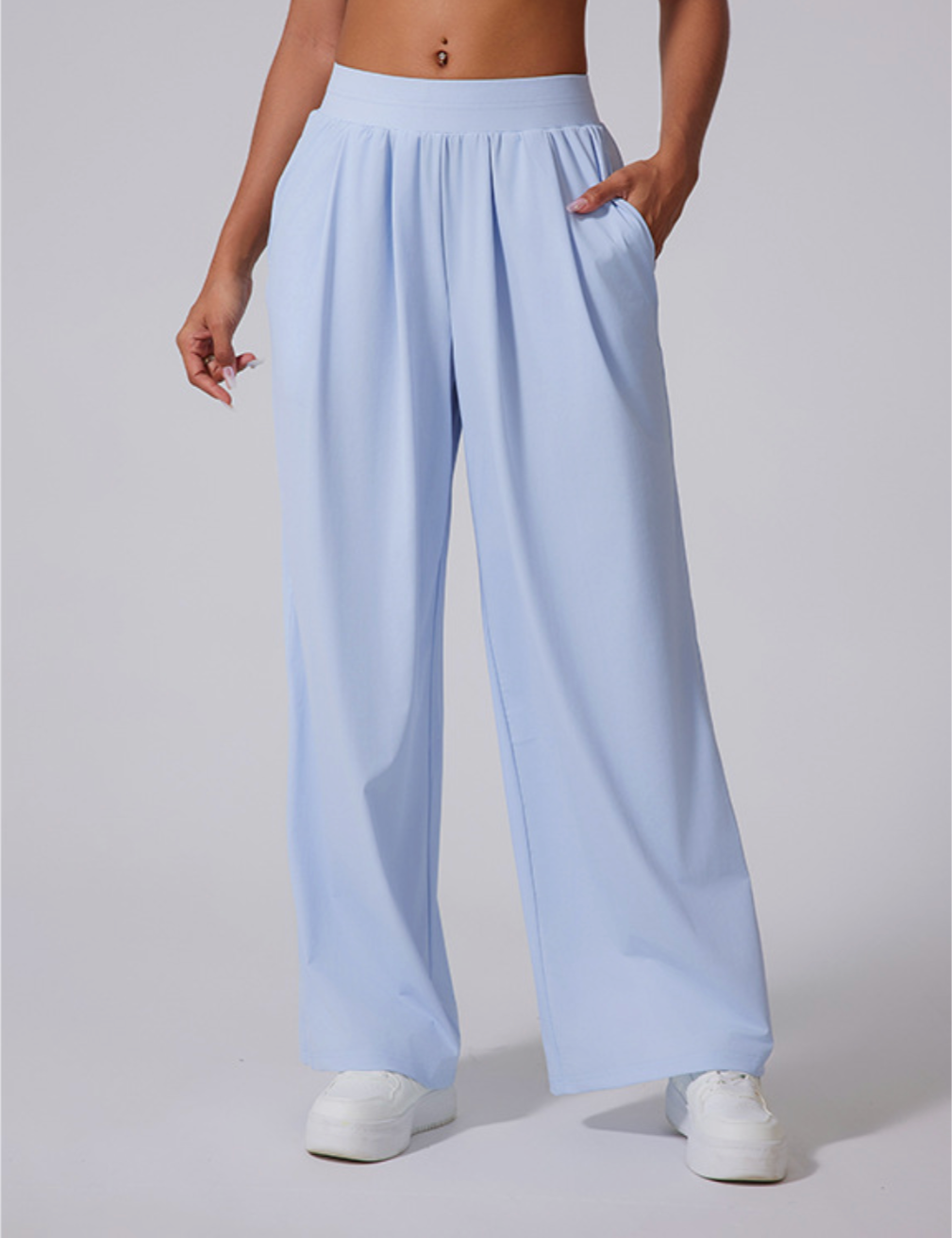 Model wearing powder blue wide-leg pants with high waistband, side pockets and pleated front, paired with white sneakers