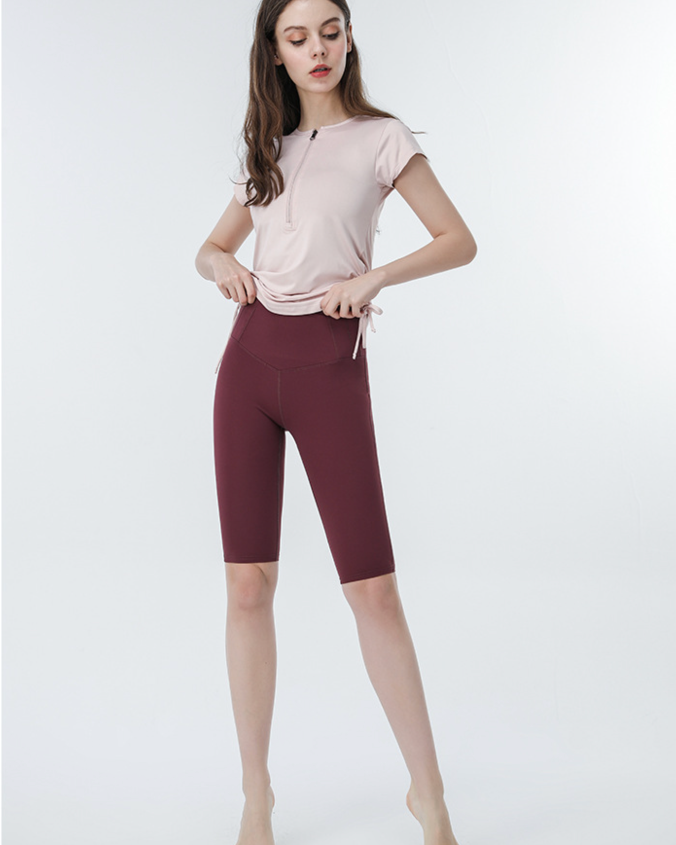Light pink active tee with drawstring sides and burgundy biker shorts, model adjusting hem