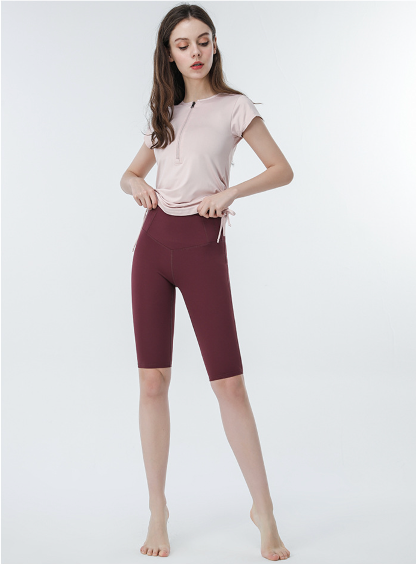 Light pink active tee with drawstring sides and burgundy biker shorts, model adjusting hem
