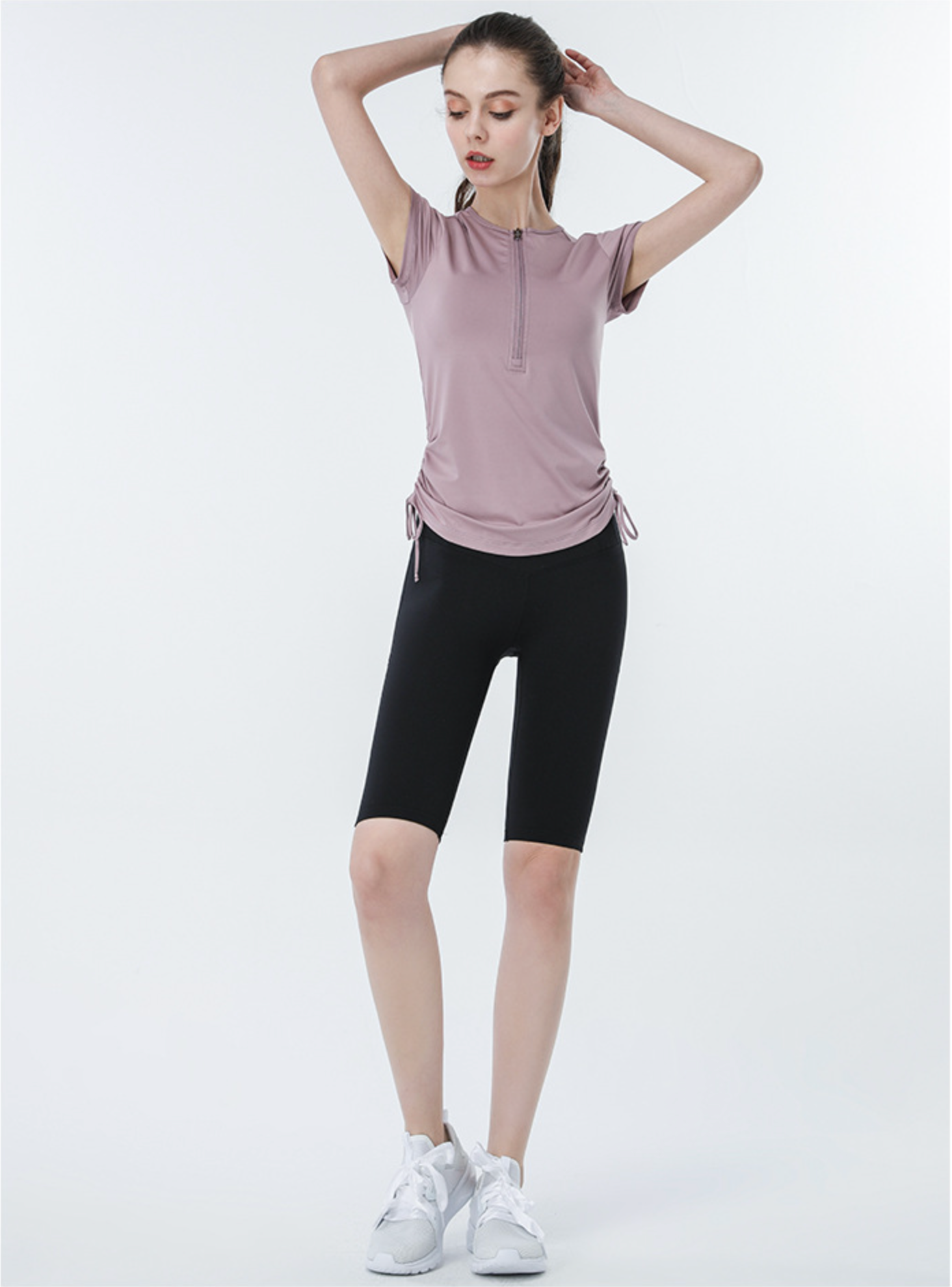 Mauve-purple active top with side ties and black biker shorts, model stretching arms overhead