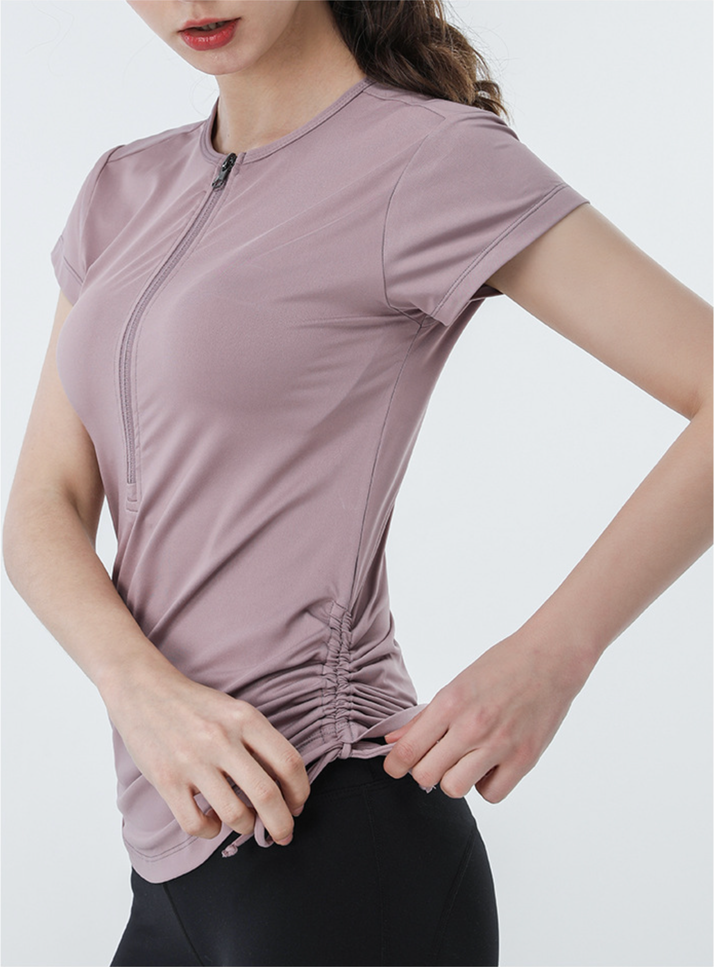 Side view of ruched drawstring top in mauve with zipper neck, model adjusting hem