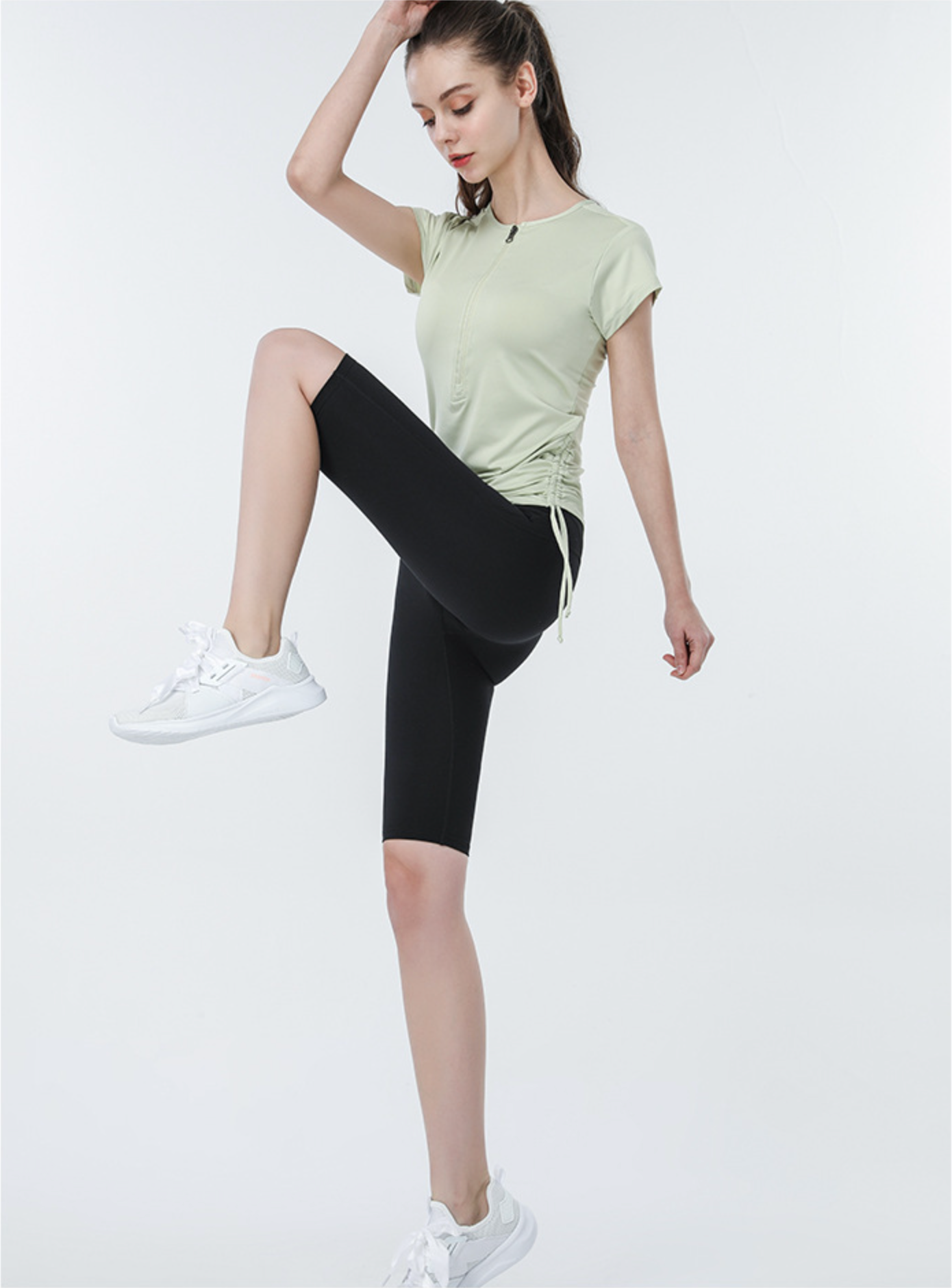 Light green zip-up sports tee with black high-rise shorts, model in active pose
