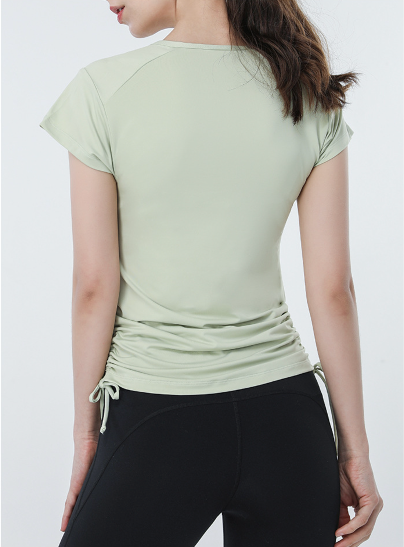 Back view of sage green active tee with ruched drawstring sides, paired with black biker shorts