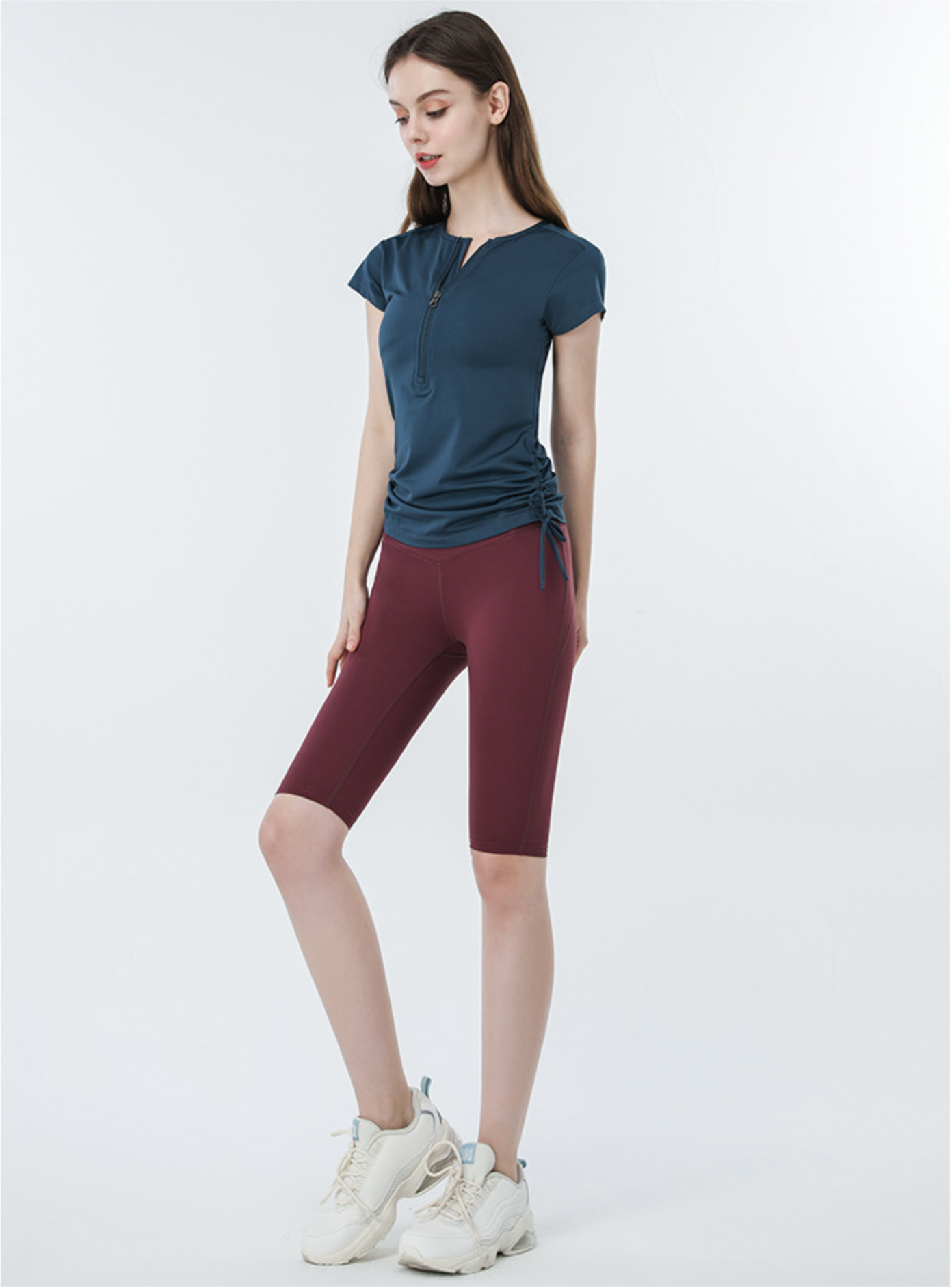 Navy blue ruched active top with burgundy cycling shorts and white sneakers, relaxed pose