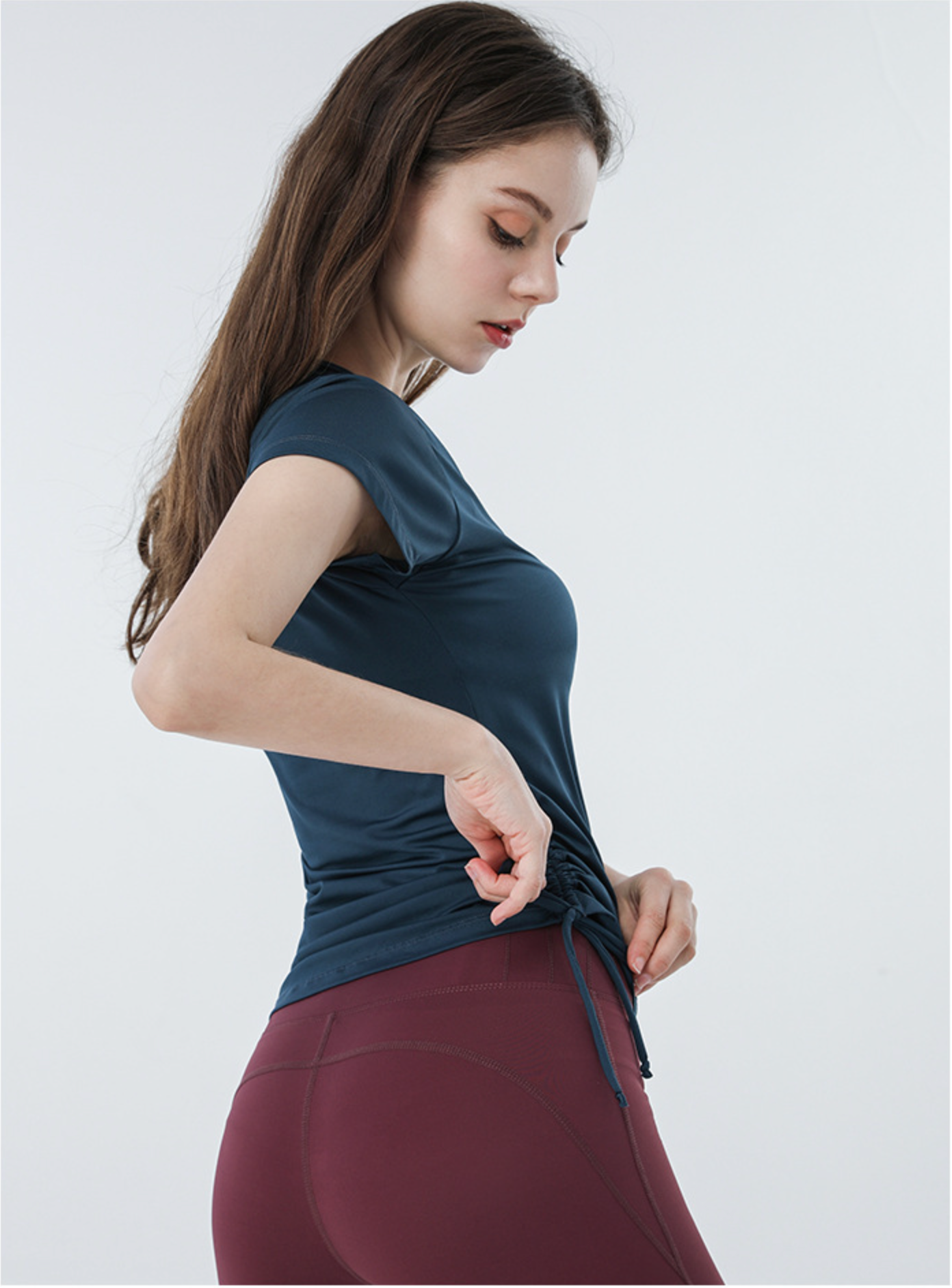 Navy blue ruched sports top with cap sleeves and high-rise burgundy biker shorts, side view pose