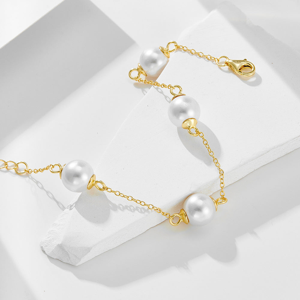 Close-up of gold pearl bracelet resting on a white geometric surface.