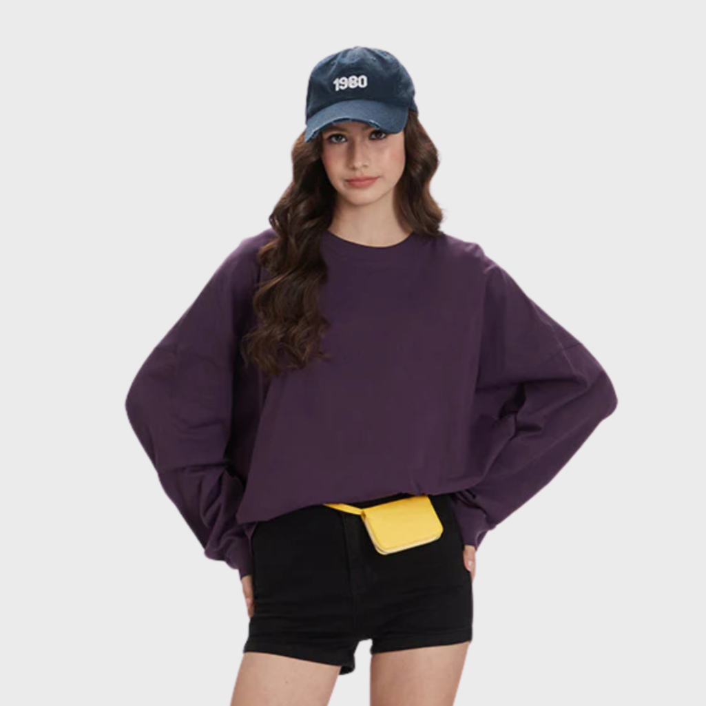 Girl in oversized purple sweatshirt, black shorts, cap and yellow sneakers