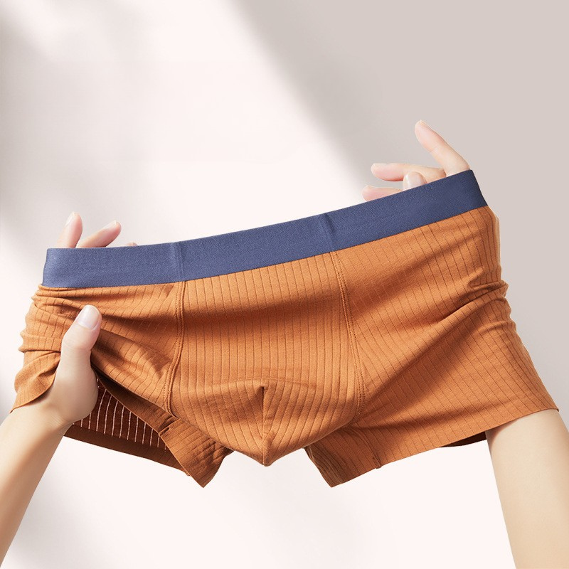 Model's hands stretching camel ribbed boxer briefs with navy waistband. Demonstrates elasticity of pinstriped underwear fabric