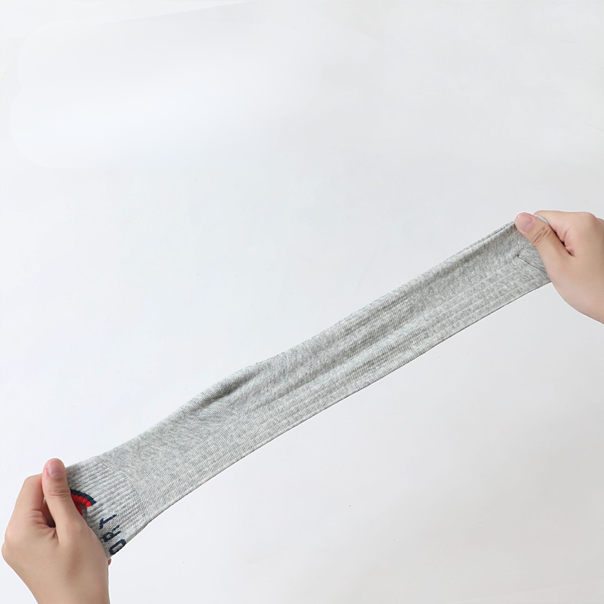 Hands stretching a gray ankle sock, showcasing its elasticity and durable fabric