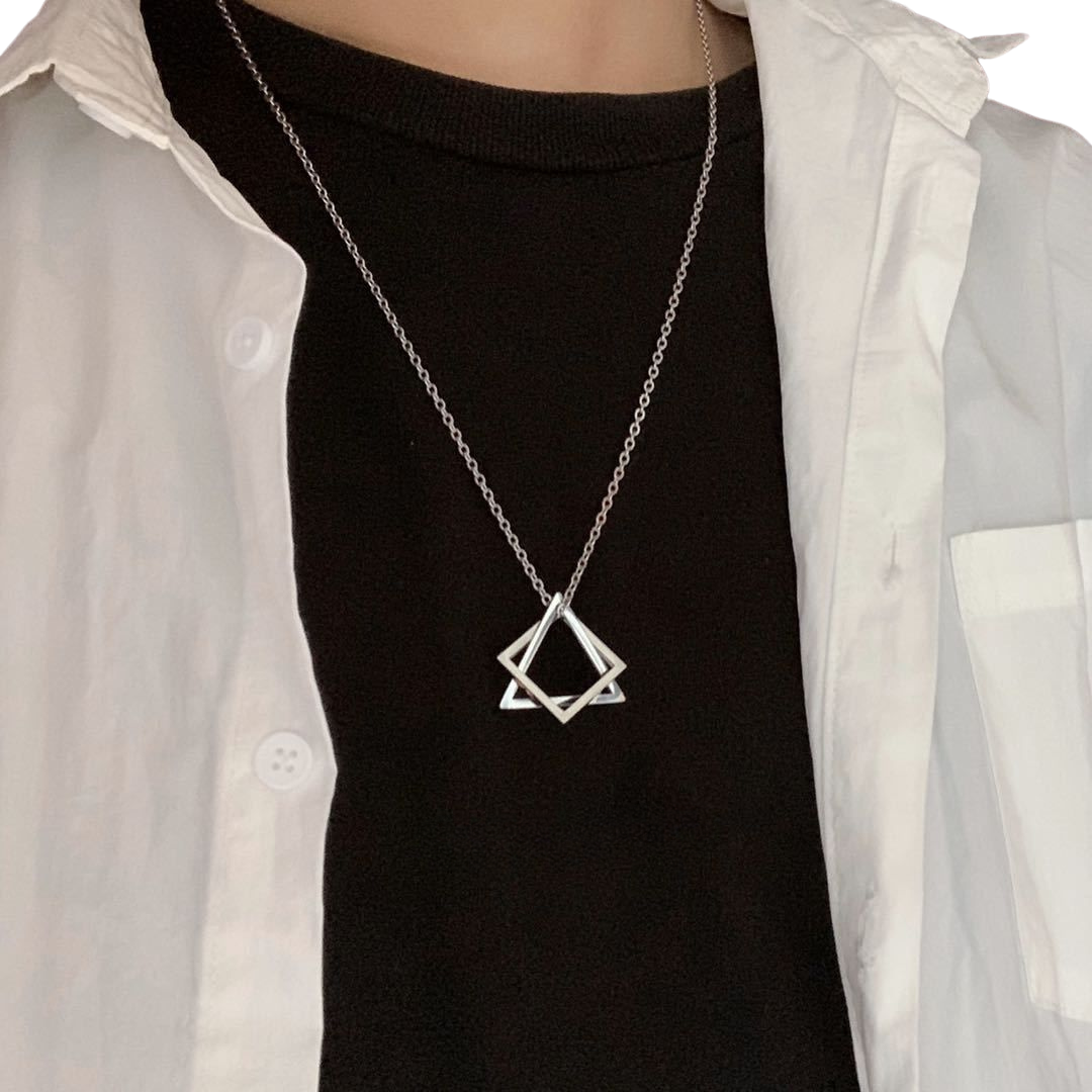 Person wearing a silver geometric pendant necklace over a black shirt with a white open button-up shirt