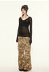 Side view of model wearing black sheer off-shoulder ribbed top styled with layered necklaces and camo pants.