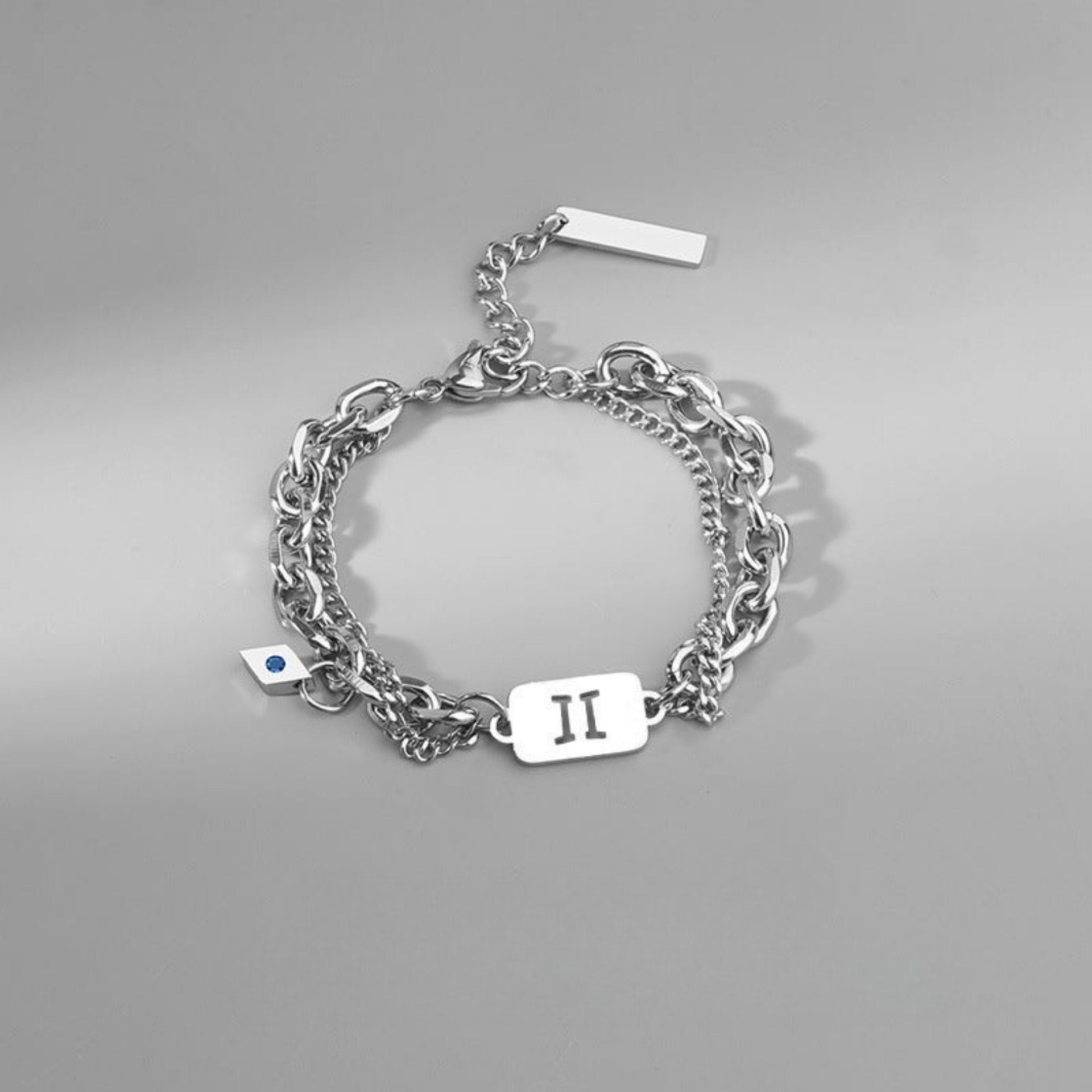 Stainless steel Gemini zodiac bracelet with layered chains and an engraved charm, displayed on a neutral background.