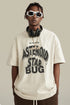 Man in cream tee with bold “Asteroid Star Bug” graphic, headphones resting on shoulders.