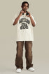 Man in cream graphic tee and brown pants holding headphones around neck.