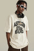 Man in cream “Asteroid Star Bug” tee looking sideways, accessorized with headphones and chain.