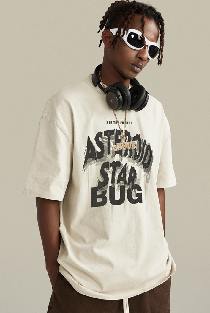 Man in cream “Asteroid Star Bug” tee looking sideways, accessorized with headphones and chain.