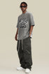 Man wearing oversized gray graphic tee and sunglasses with relaxed pose.
