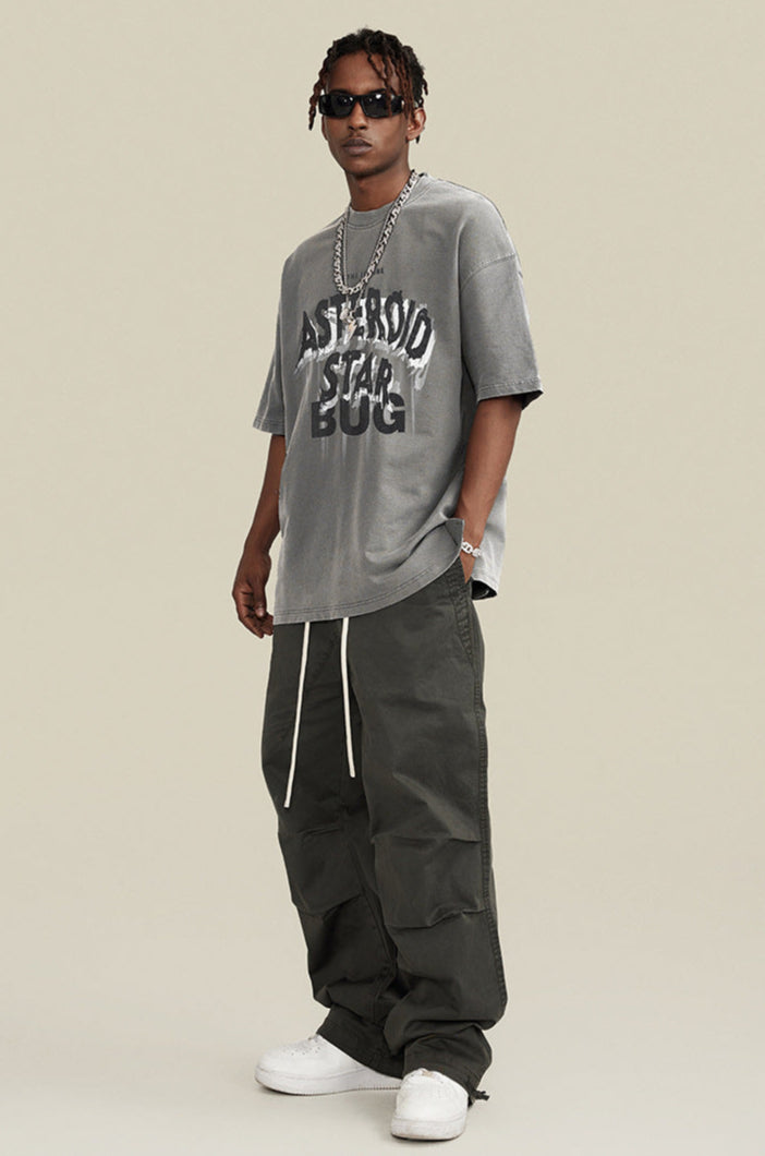 Man wearing oversized gray graphic tee and sunglasses with relaxed pose.