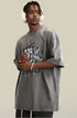 Man in gray tee with headphones and layered jewelry clasping hands in front.