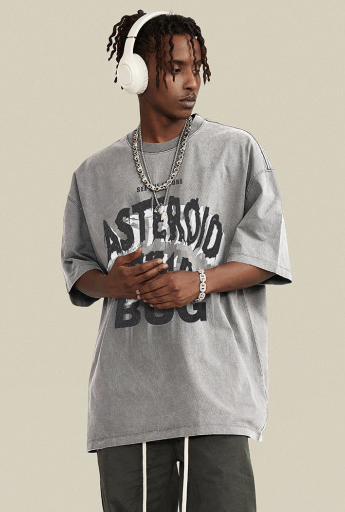 Man in gray washed tee wearing white headphones, looking sideways with layered chains.