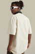 Man turned away in oversized cream tee styled with brown pants.

