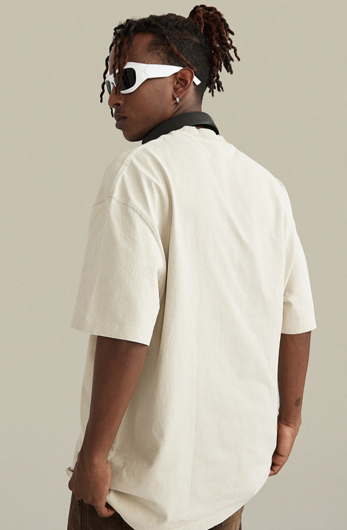 Man turned away in oversized cream tee styled with brown pants.


