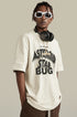 Man wearing cream graphic tee with “Asteroid Star Bug” print, headphones around neck.