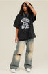 Model wears oversized black graphic tee with distressed jeans and white sneakers.