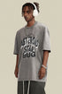 Man wearing oversized gray tee with bold “Asteroid Star Bug” print and layered chains.
