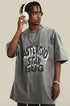 Man adjusting white headphones in gray graphic tee with streetwear chains.