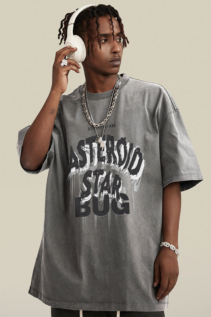 Man adjusting white headphones in gray graphic tee with streetwear chains.