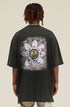 Model showing back of black tee with large daisy and cartoon face design.