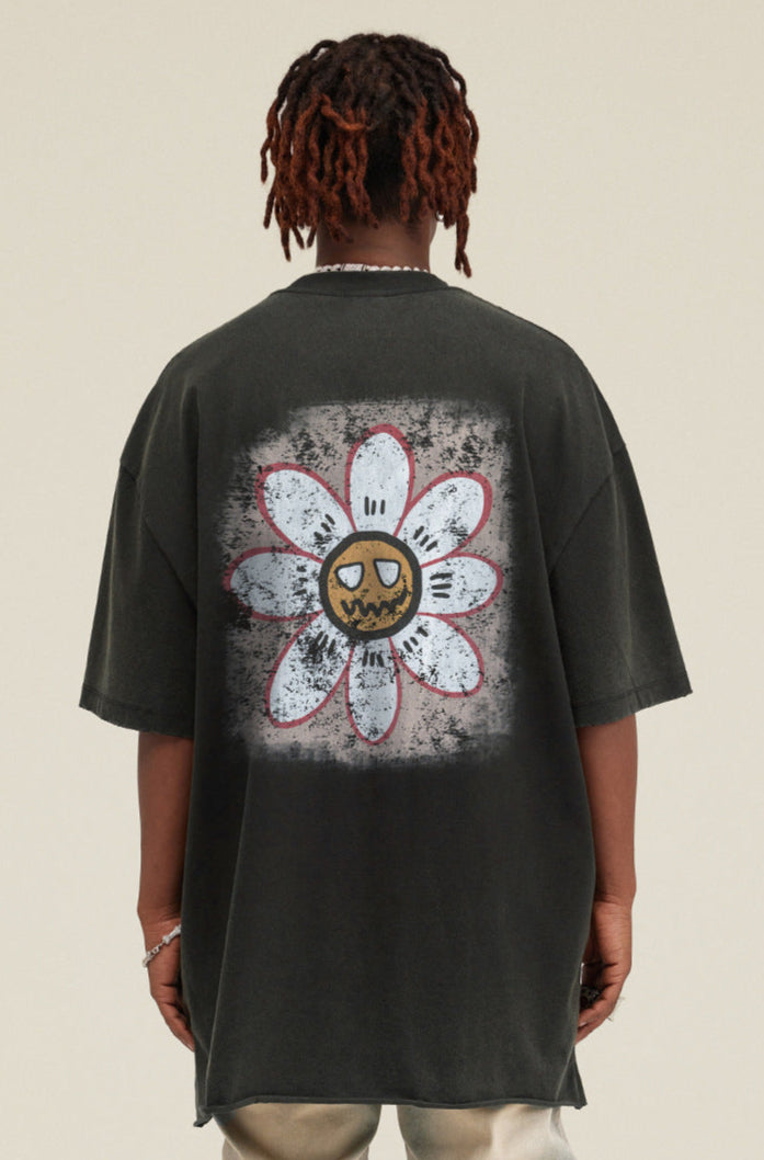 Model showing back of black tee with large daisy and cartoon face design.