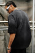 Back view of man in black oversized tee with washed texture and braided hair.