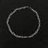 Silver barbed wire necklace with twisted chain laid flat on black background.